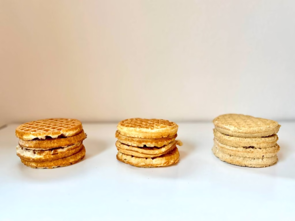 The photo shows three stacks of waffles. Each waffle has a square grid pattern, and the stacks are arranged from left to right. The two stacks on the left are golden-brown, and the one on the right is a lighter tan.