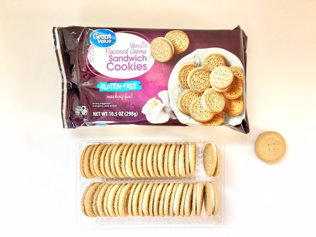 A sealed package of "Great Value Vanilla Flavored Crème Sandwich Cookies" is displayed at the top of the image. The packaging is dark brown and features an image of the cookies on a white plate next to a vanilla flower. Prominently displayed is "GLUTEN-FREE snacking fun!" Below the sealed package, an opened clear plastic tray of the same "Great Value" cookies is shown. The tray contains two rows of stacked vanilla sandwich cookies with white cream filling. To the right of the open tray, a single loose cookie is visible. The background is a plain white surface.